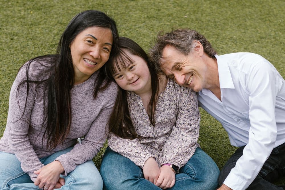 A young woman with Down syndrome relaxing on the grass with two people close to her