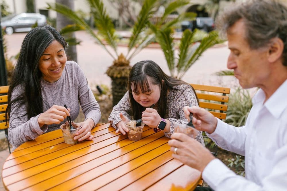 A young woman with Down syndrome enjoying a treat at a café table with two adults