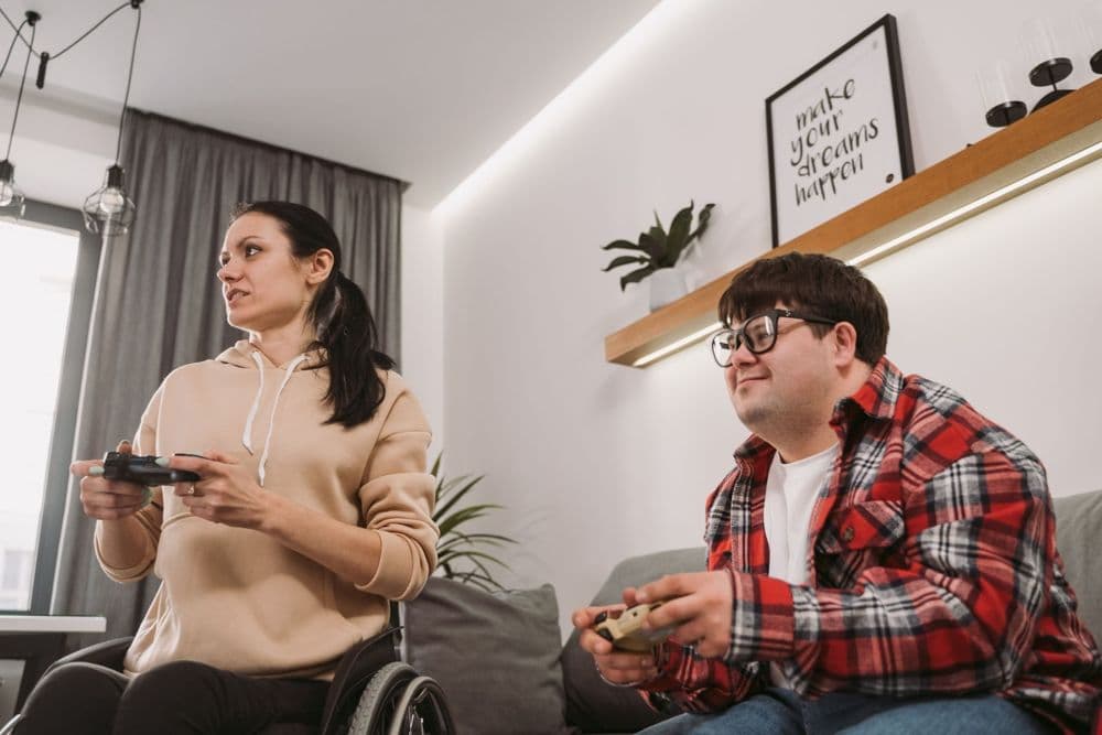 A woman who uses a wheelchair and a young man with Down syndrome playing video games together