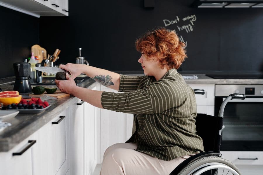 A woman who uses a wheelchair slicing food at her kitchen counter