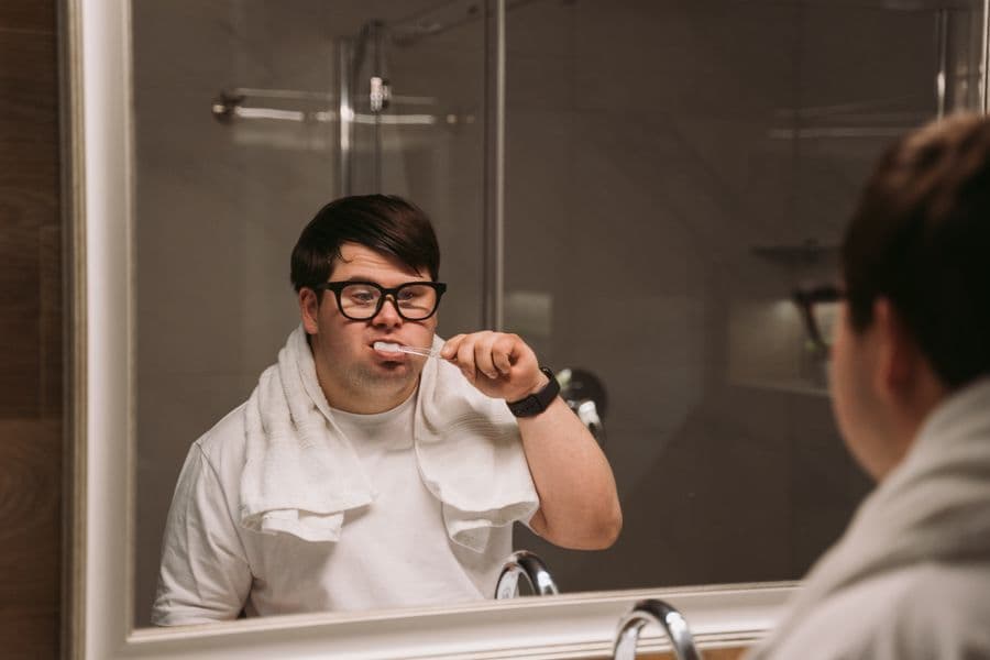 A young man with Down syndrome brushing his teeth at the mirror